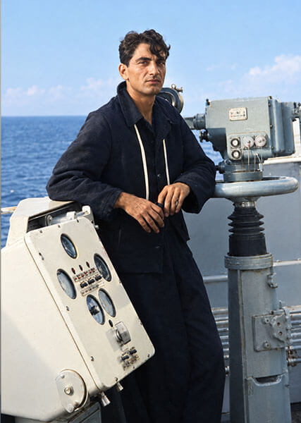 Ritratto di Vittorio Russo in divisa scura a bordo dell'incrociatore Andrea Doria, appoggiato alle apparecchiature di navigazione e puntamento durante la traversata dell'Oceano Indiano nell'ottobre 1964.